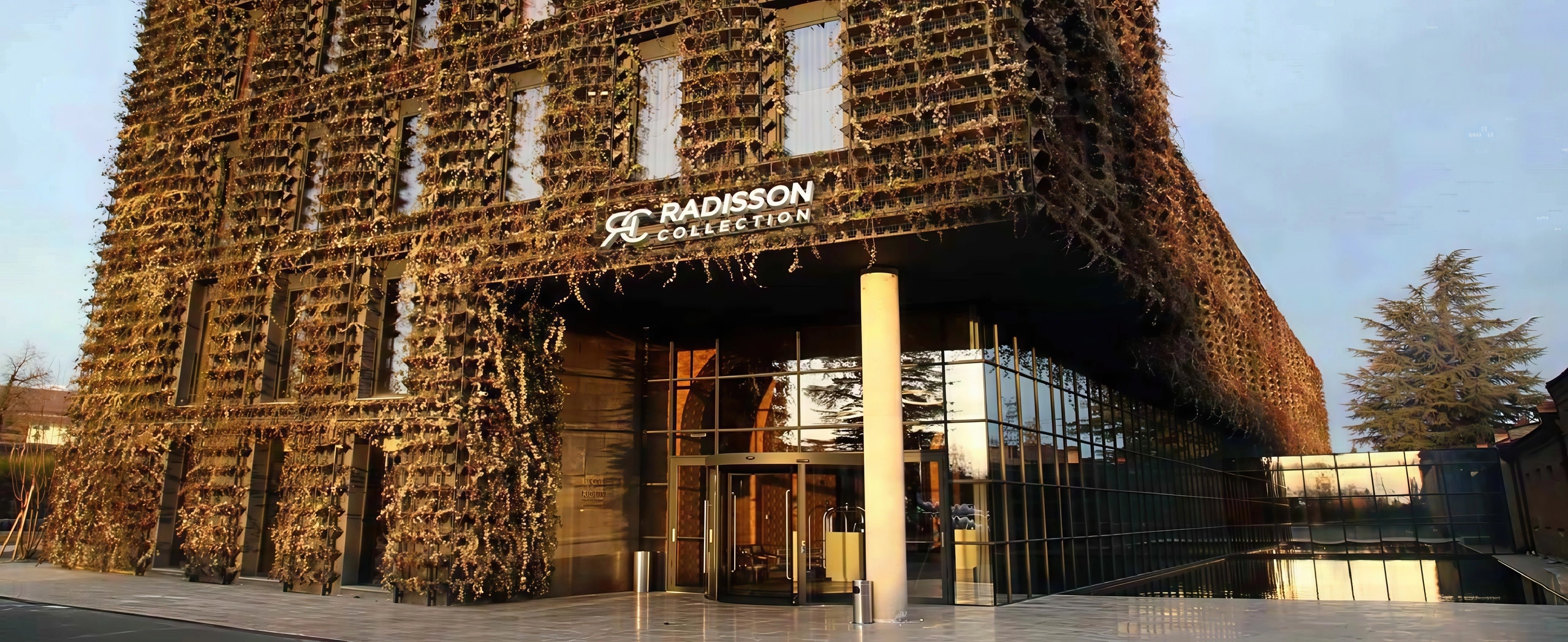 Exterior of Radisson Collection hotel featuring a modern glass structure covered with vertical green elements and decorative facade panels, photographed in warm daylight.